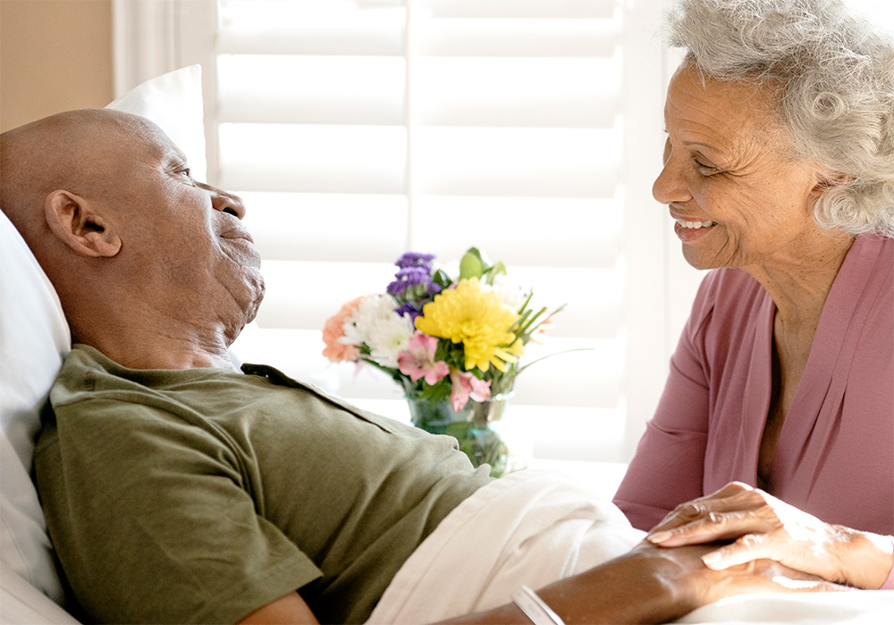 Woman holding hand of man in hospital with flowers on the table
