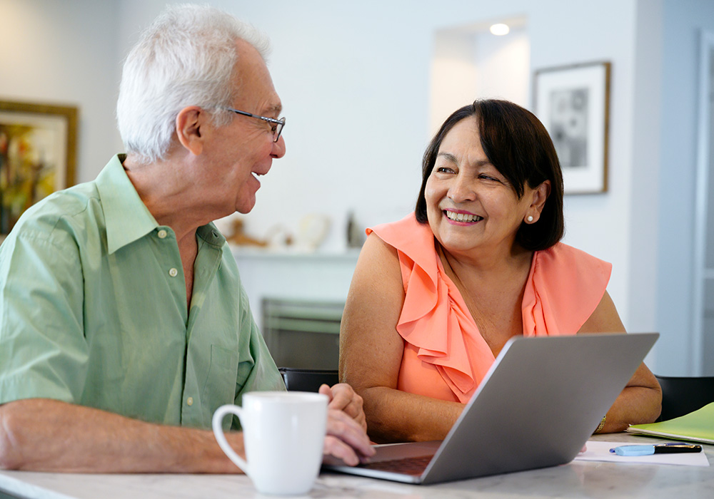 A couple in spring colored clothing sitting in front of computer and smiling