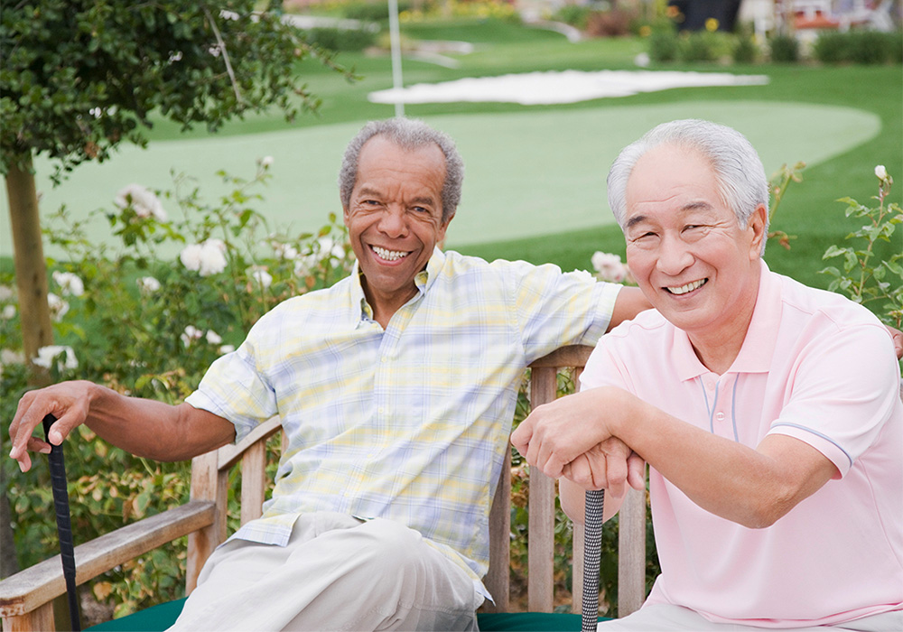 Two gentlemen sitting on a bench next to putting green