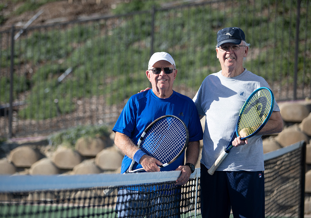 two elderly gentlemen standing at the net holding tennis racquets