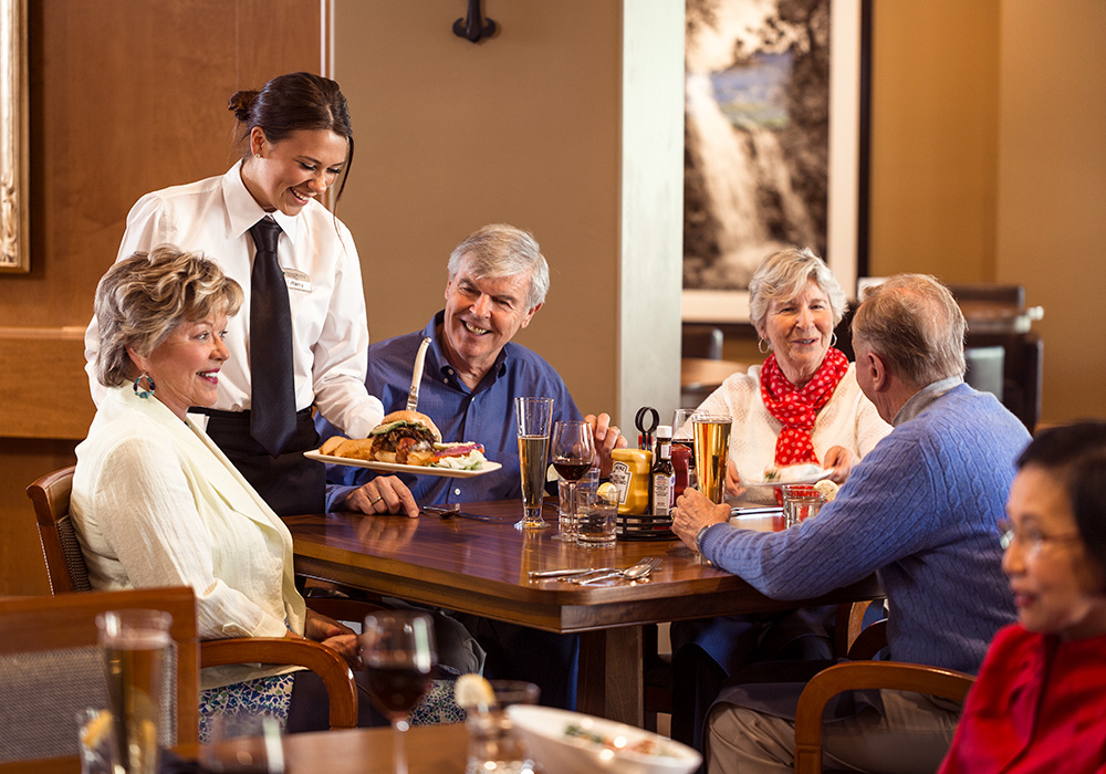 two mature couples in the dining area being served lunch by a young server