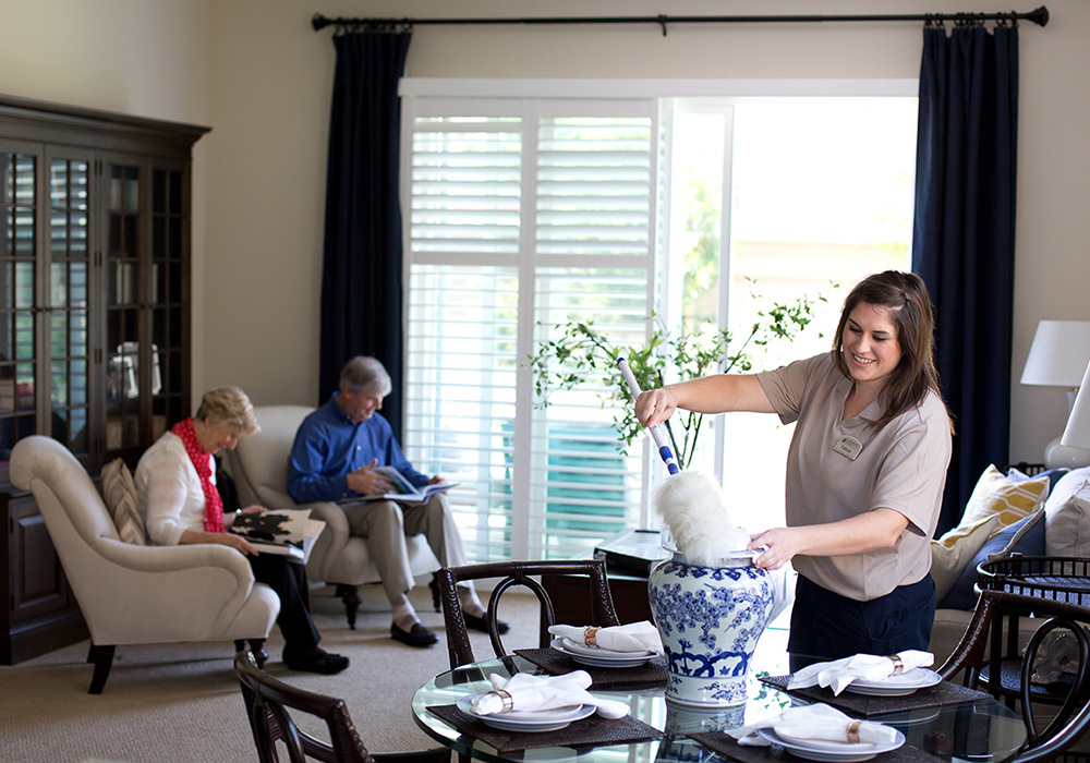 a woman cleaning a home with a couple sitting and reading