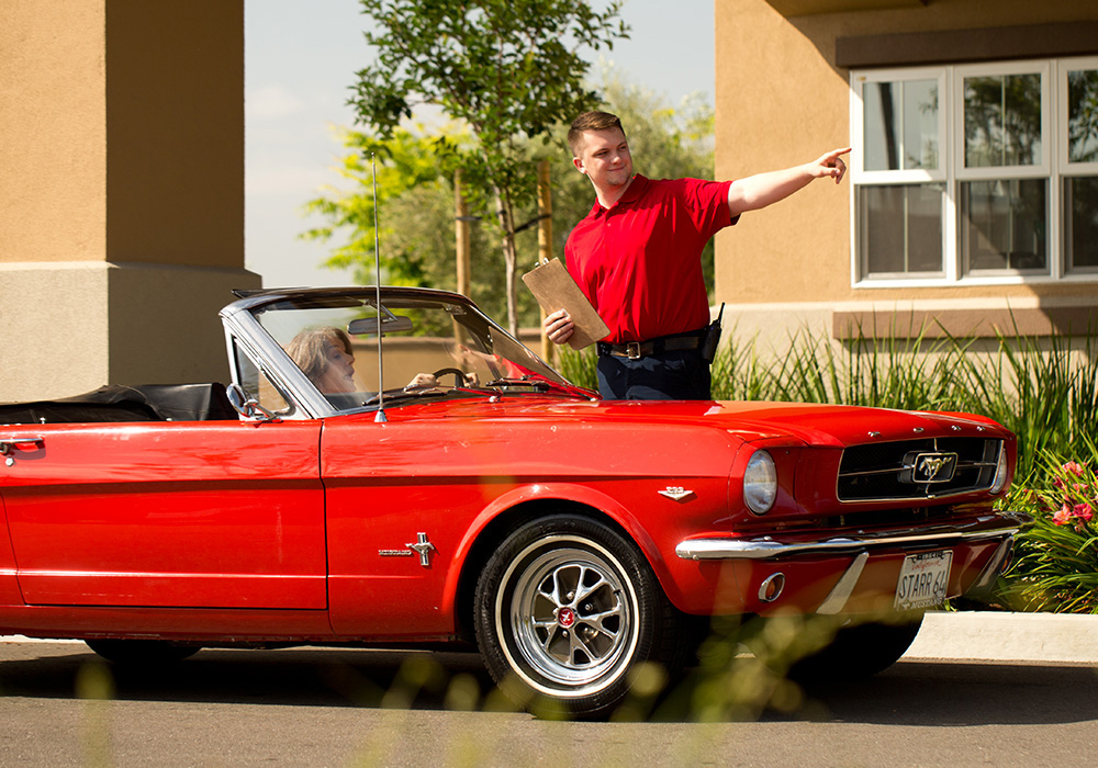 A woman driving a red mustang convertible at the gated security kiosk