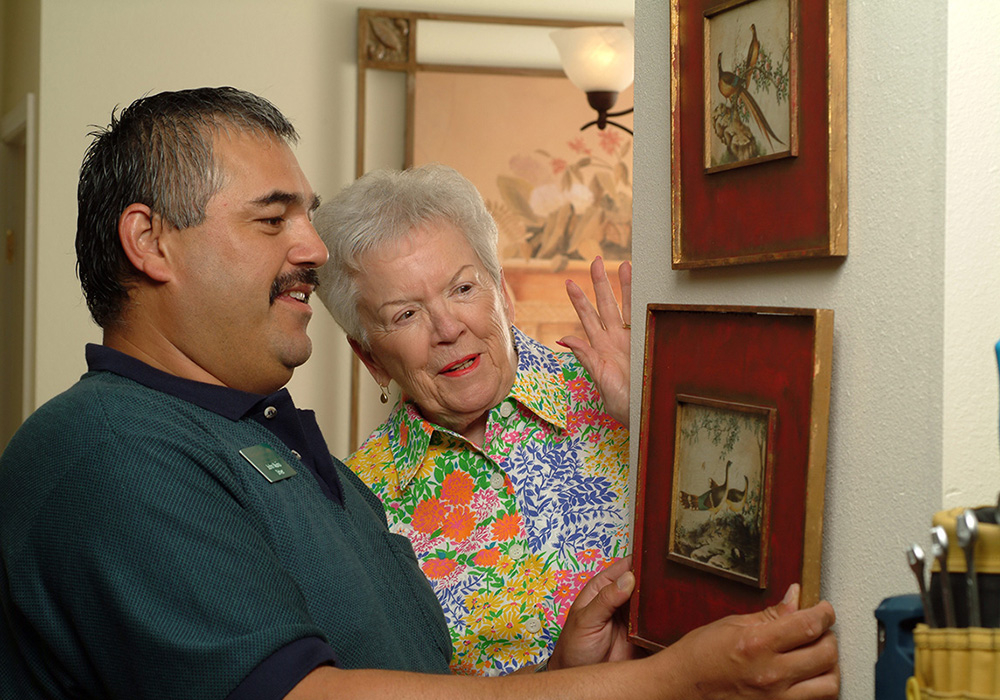 A handyman helping a mature woman hang a picture on the wall