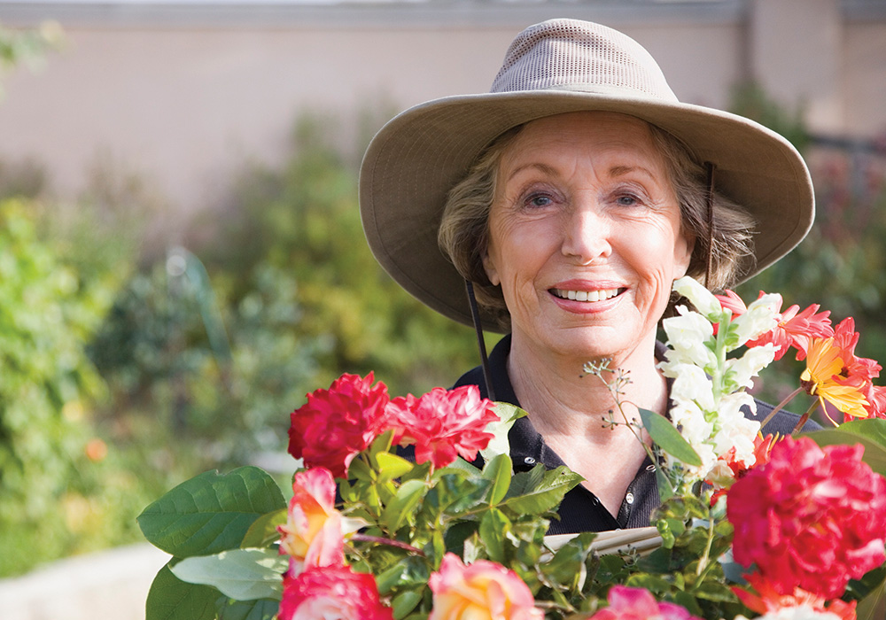 Woman outdoors with hat on behind flowers