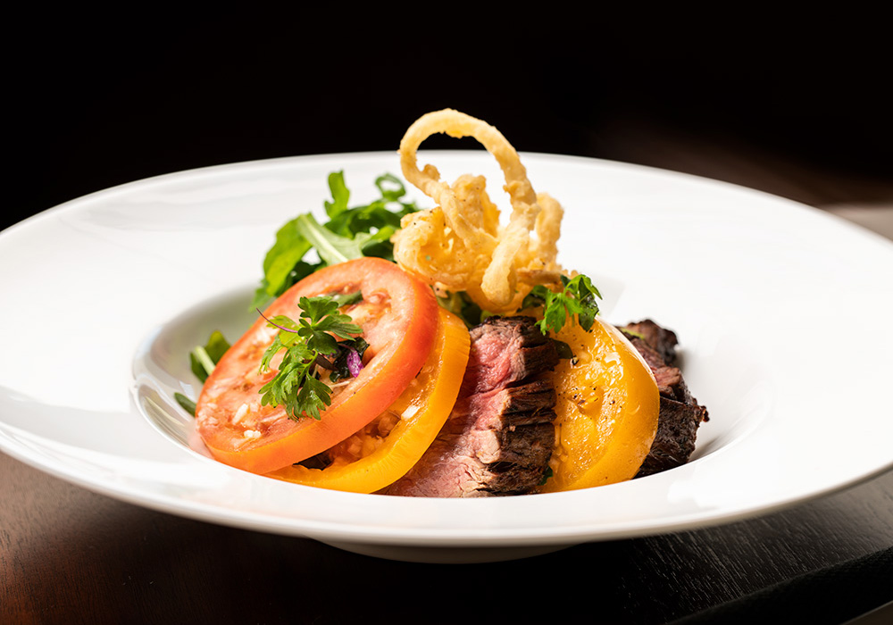 food sitting on a plate Gourmet beef and sliced tomatoes.