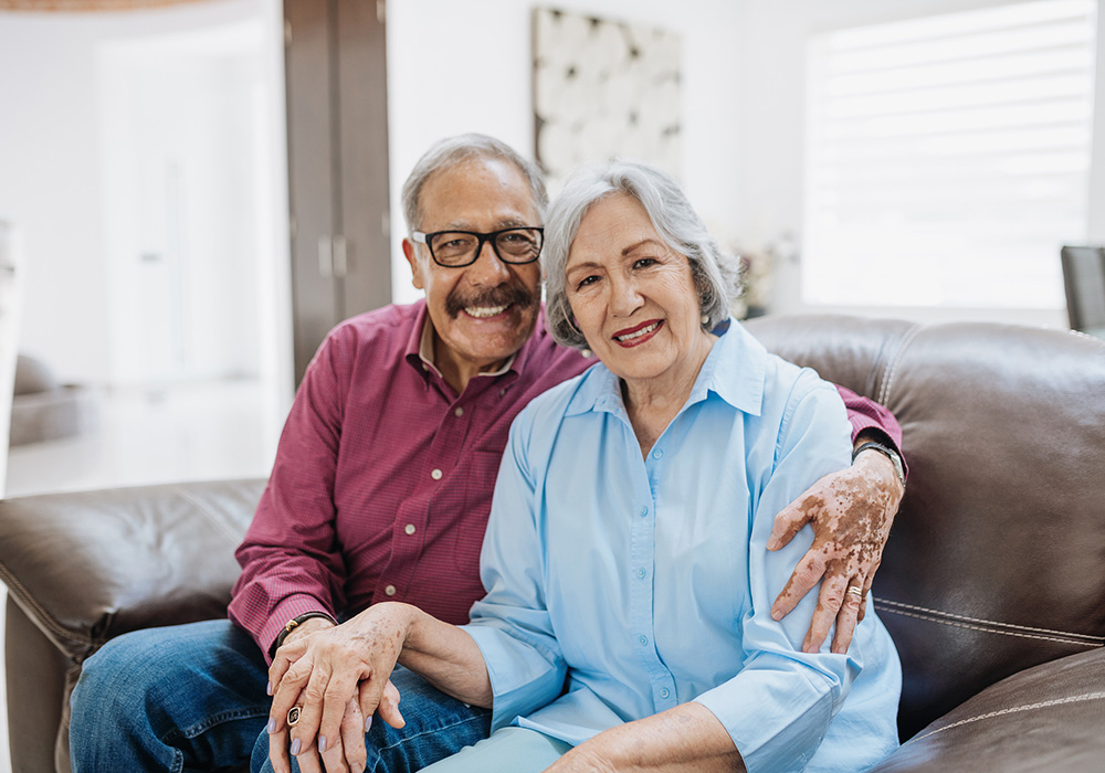 Senior couple sitting on a leather sofa embracing and smiling
