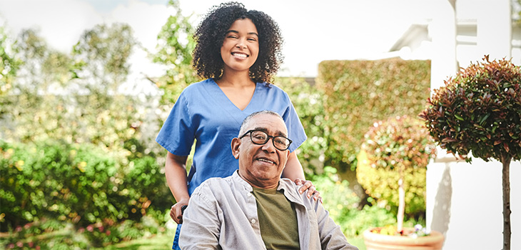 An African American nurse pushing an African American elderly man in a wheelchair outdoors