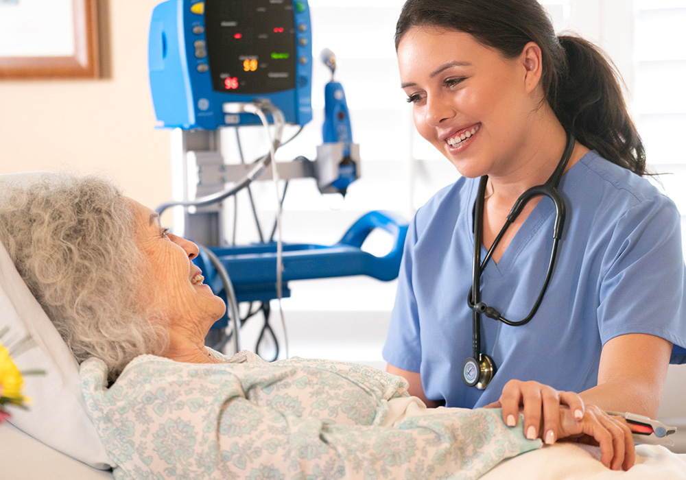 parkvista-1000x700-2 Caregiver talking to woman in hospital bed.
