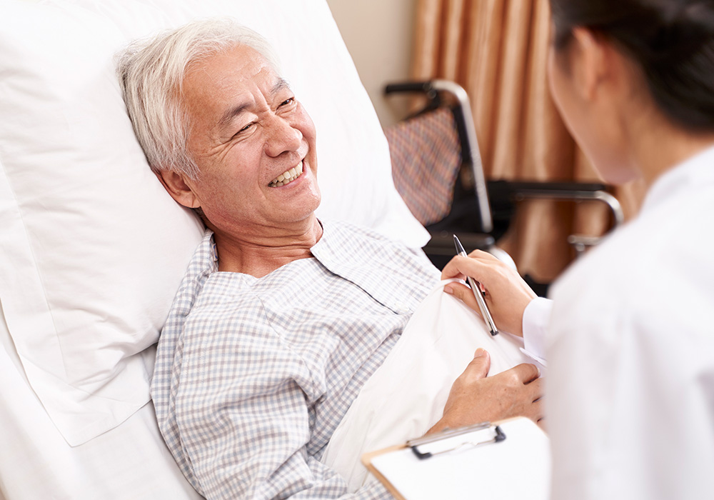 parkvista-1000x700-34 Man smiling in hospital bed talking to a doctor with clipboard