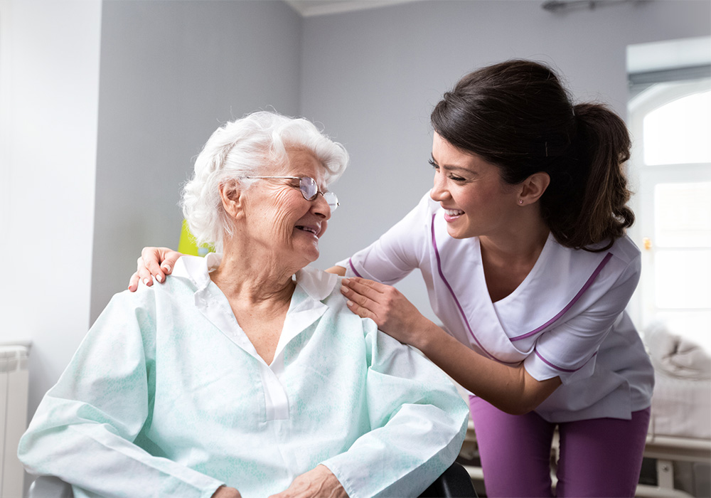 Healthcare worker in purple scrubs with an elderly woman in a chair
