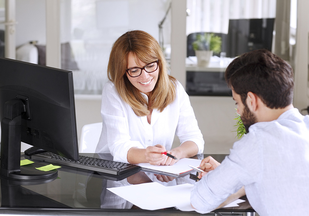 Woman in front of computer reviewing papers with man