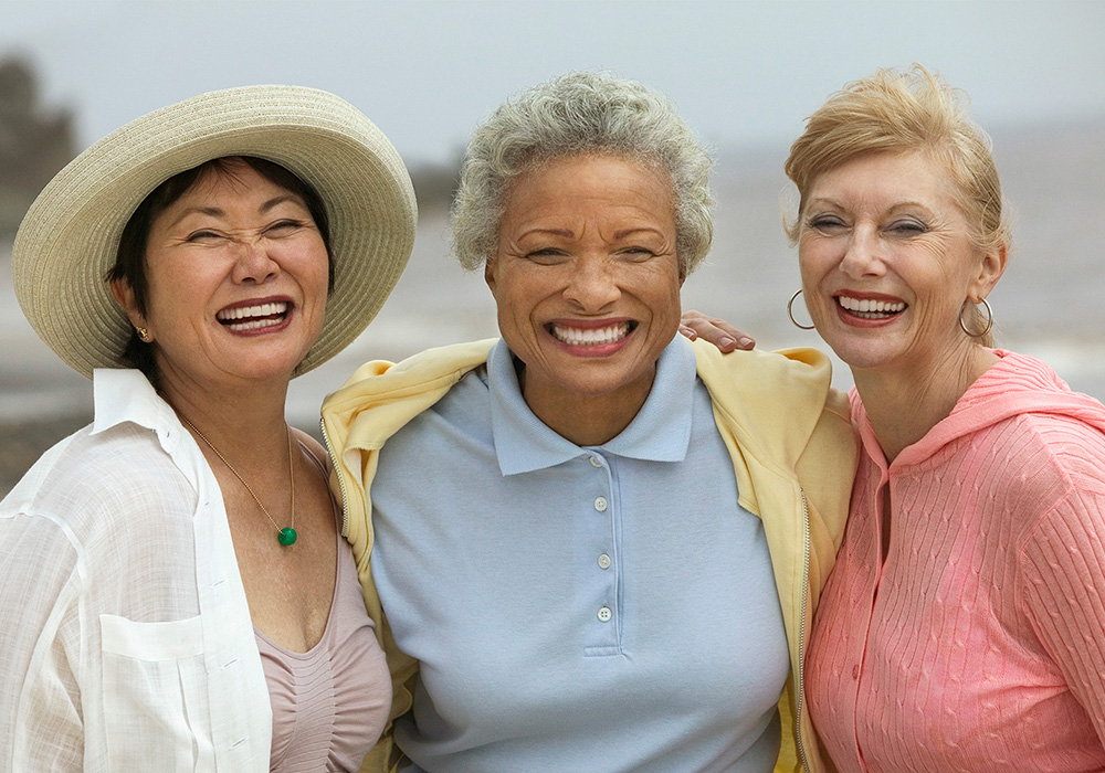 Three women in pastel colored clothes smiling on the beach