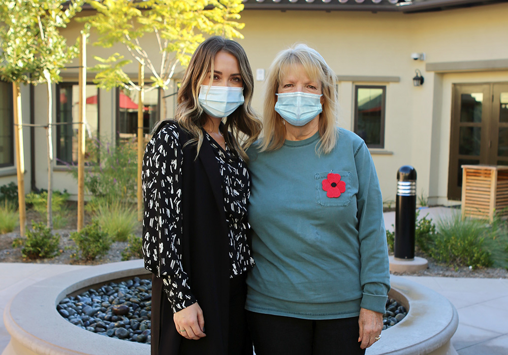 Two women with masks on in front of The Orchards