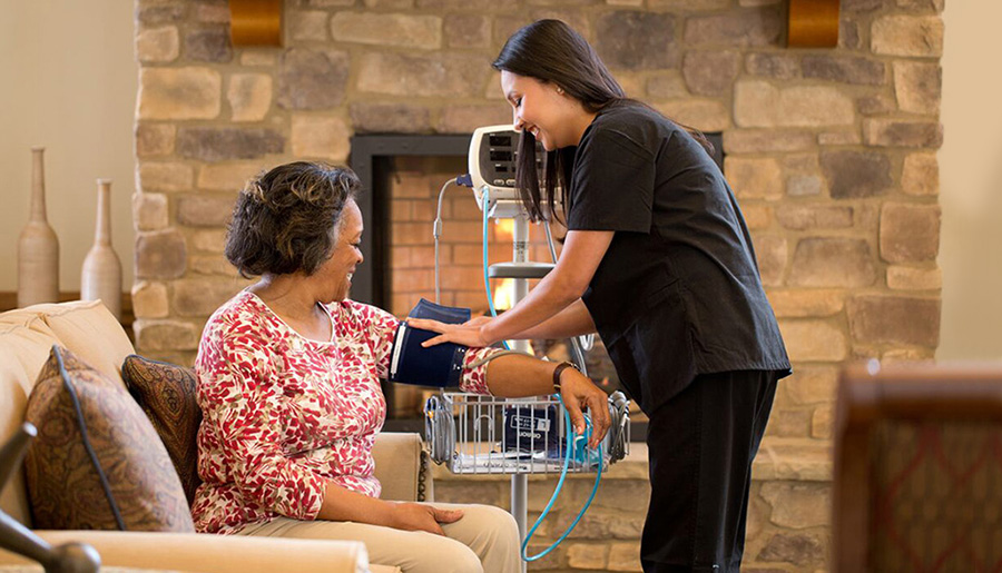 A nurse taking the vitals of a senior woman sitting in a chair in front of her. A nurse taking the vitals of a senior woman sitting in a chair in front of her.