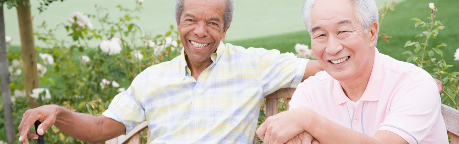 Two senior men sitting on a bench with golf clubs in their hands.
