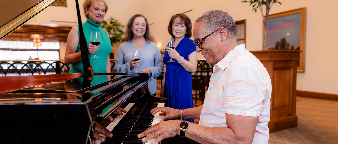 A gentleman playing a piano with a few women listening