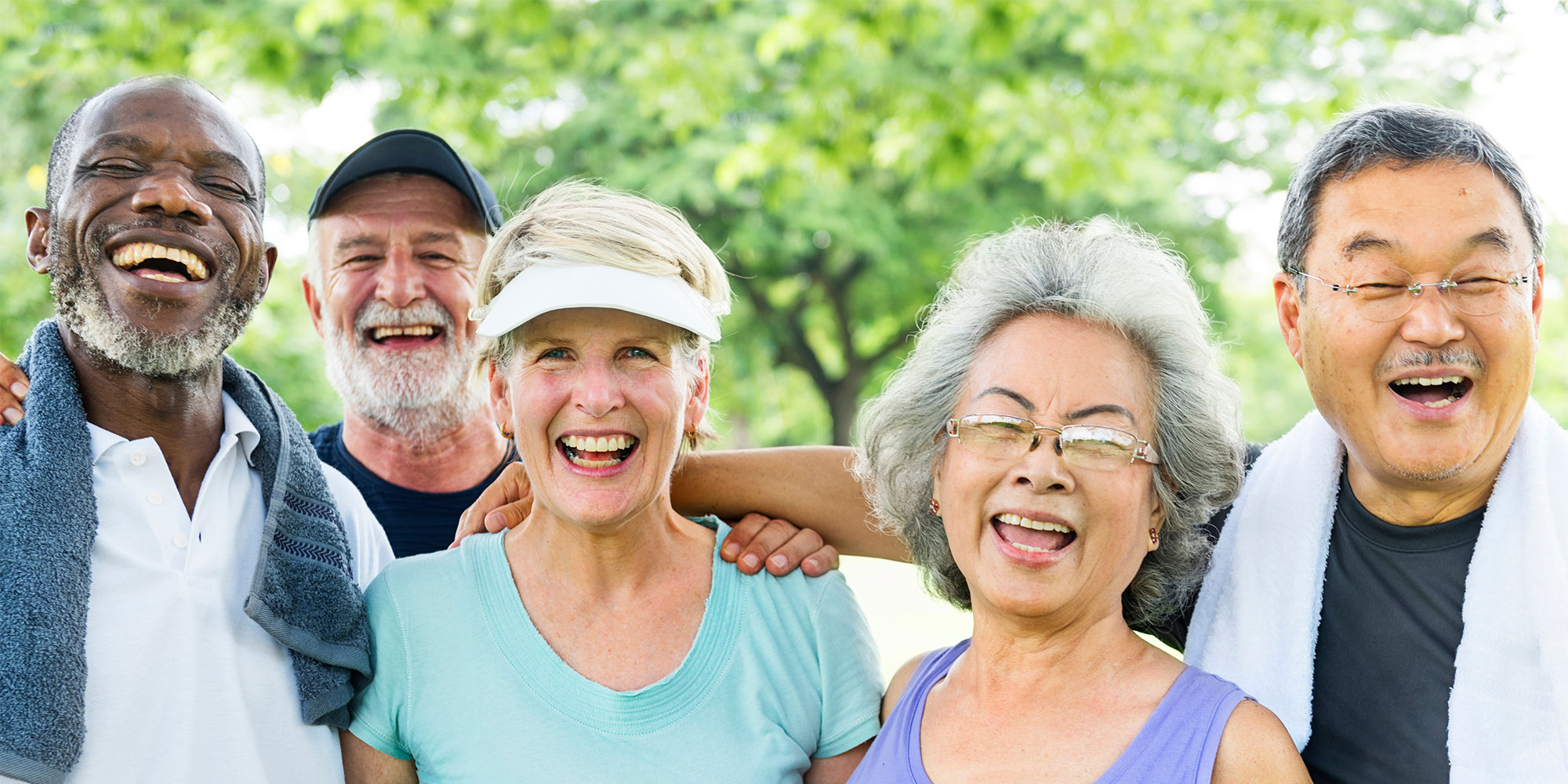 A group of seniors smiling outside under a large tree.